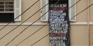 Após ser fotografada nua dentro de casa, mulher expõe grande faixa com Código Penal na janela